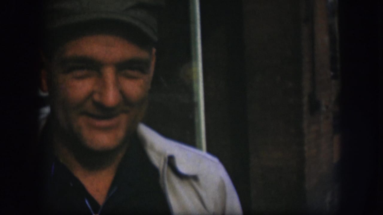 A man in a dark cap faces the camera in this 1958 Kansas home-movie frame, standing near wood trim and interior fixtures.