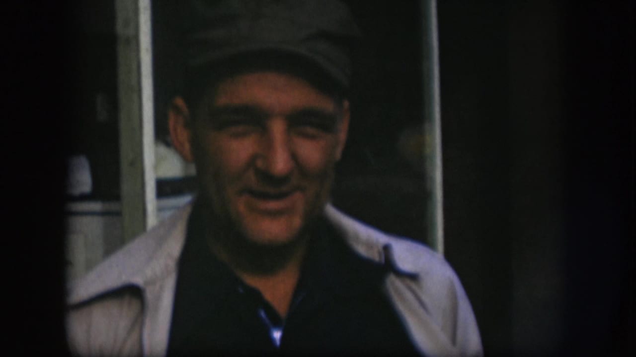 Man in a dark cap and light jacket facing the camera in dim light.