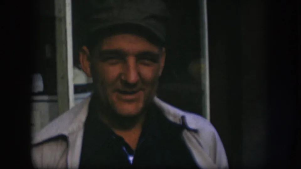 Adult man in Kansas 1958 home-movie footage faces the camera while wearing a dark cap, dark shirt, and light jacket.