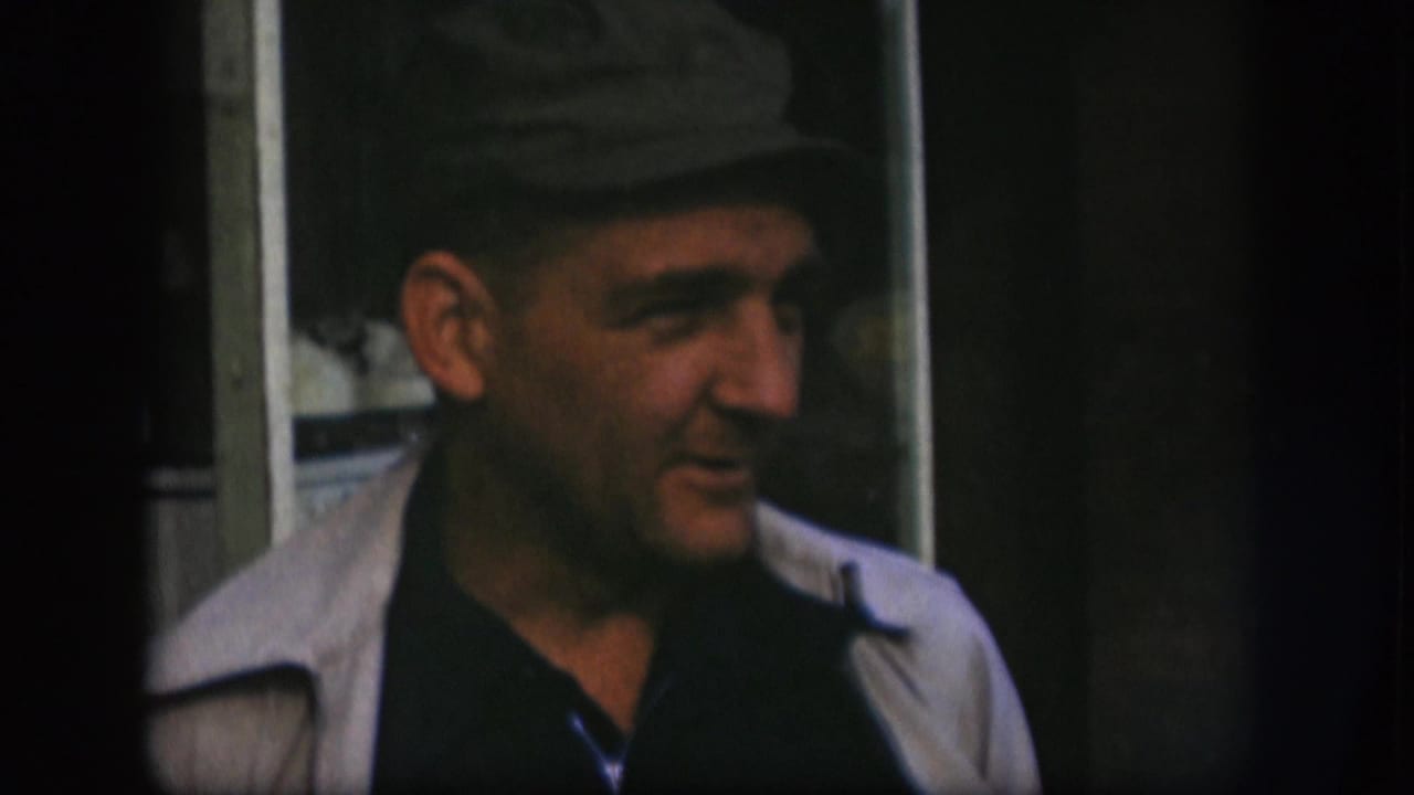 Adult man in a dark cap and light jacket turns to his right during a 1958 Kansas 8mm home-movie shot.