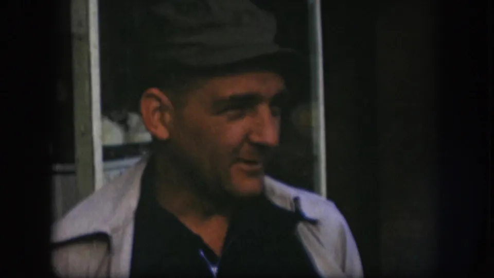 Adult man in a dark cap and light jacket turns to his right during a 1958 Kansas 8mm home-movie shot.