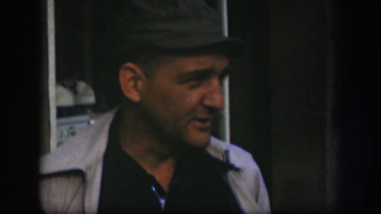 Kansas 1958 home-movie frame shows the man in side view, wearing a dark cap, dark shirt, and light jacket.