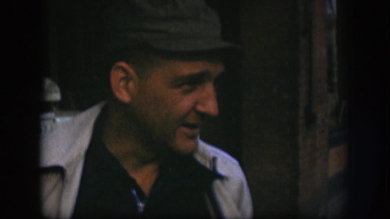 Adult man in 1958 Kansas footage smiles in side profile while standing near a dark doorway or window frame.