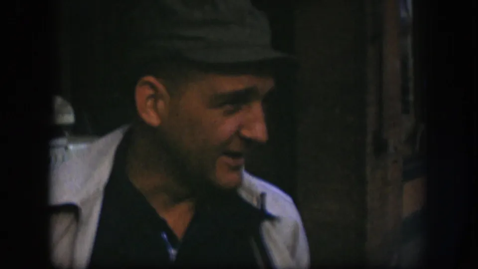 Adult man in 1958 Kansas footage smiles in side profile while standing near a dark doorway or window frame.