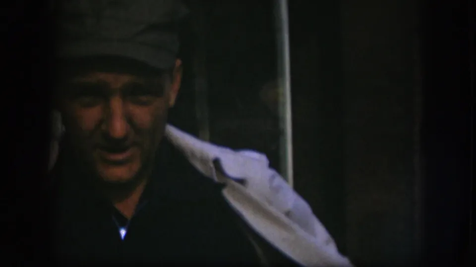 In this 1958 Kansas frame, the man appears lower in the shot, his cap, dark shirt, and light coat visible in dim light.