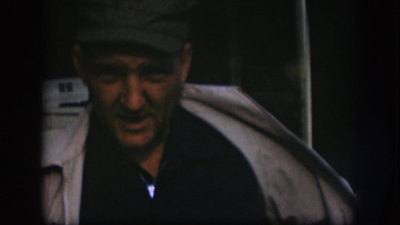 The man leans forward in the final 1958 Kansas 8mm frame, with his light coat draped open and face partly shadowed.