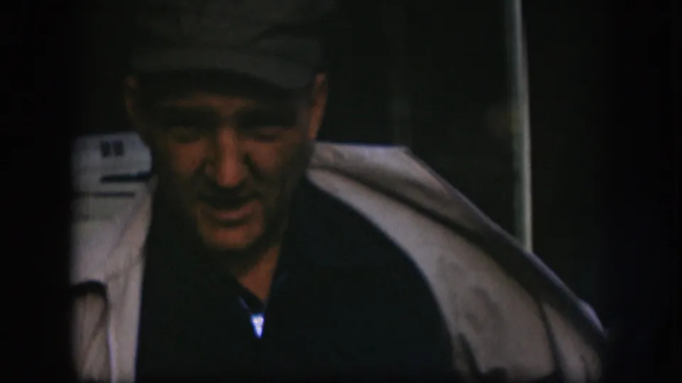 The man leans forward in the final 1958 Kansas 8mm frame, with his light coat draped open and face partly shadowed.