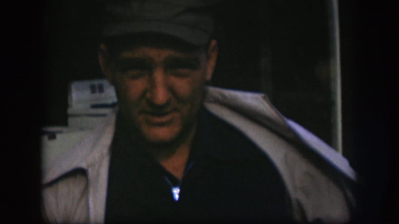 Man in a cap and light coat stands in a dark interior or doorway.