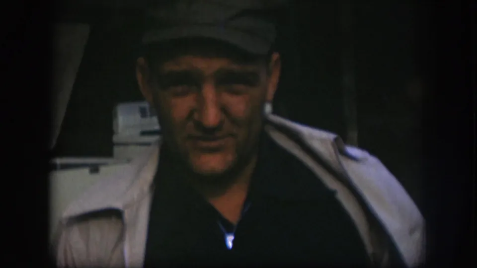 Close view of an adult man wearing a cap and light coat, filmed with soft 8mm grain in Kansas, 1958.