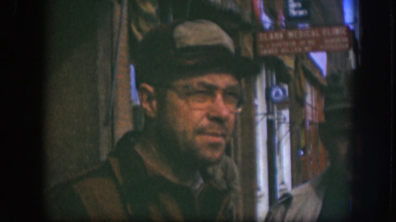 Adult man in glasses, a cap, and dark coat stands on a Kansas sidewalk near a red Clark Medical Clinic sign, 1958.