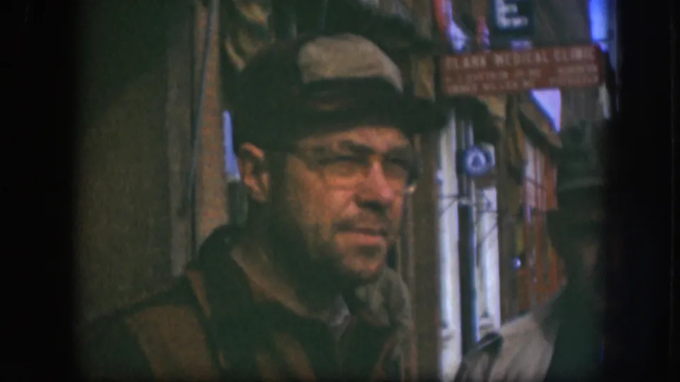 Adult man in glasses, a cap, and dark coat stands on a Kansas sidewalk near a red Clark Medical Clinic sign, 1958.