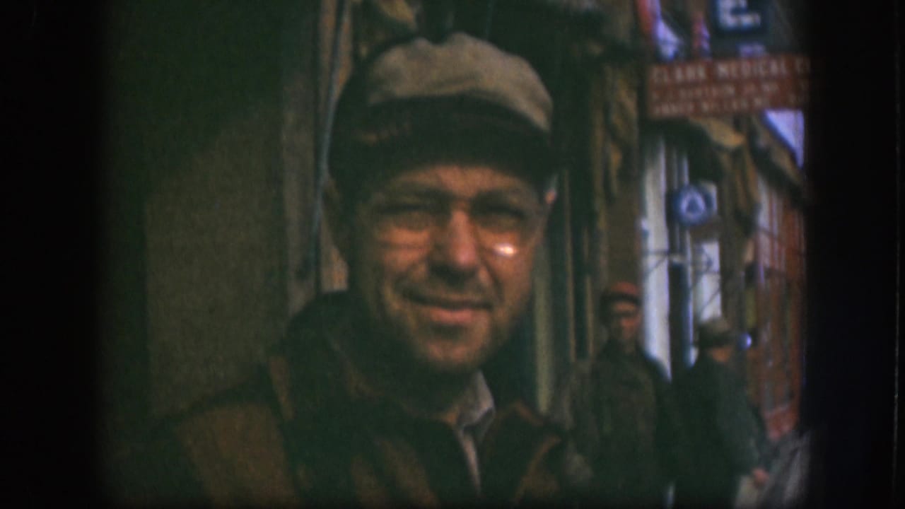 Man in cap and glasses smiles toward the camera in a narrow street passage.