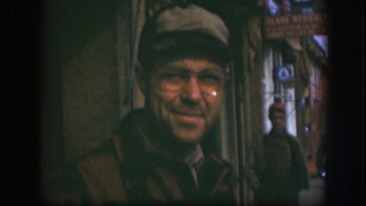 A 1958 Kansas street view shows the man in cap and glasses near the lens, with signage and background pedestrians partly visible behind him.