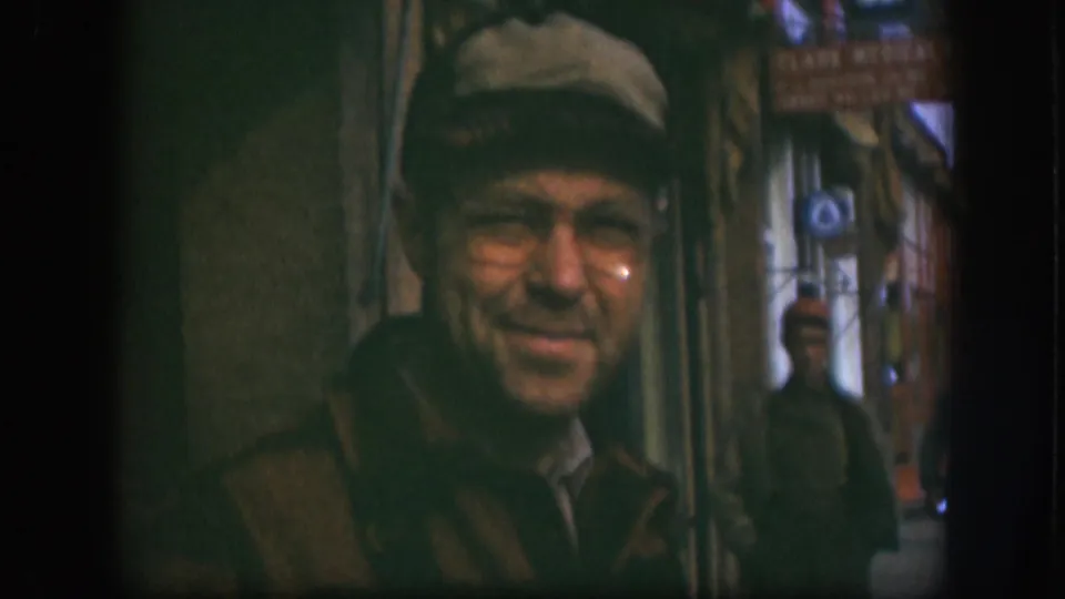 A 1958 Kansas street view shows the man in cap and glasses near the lens, with signage and background pedestrians partly visible behind him.