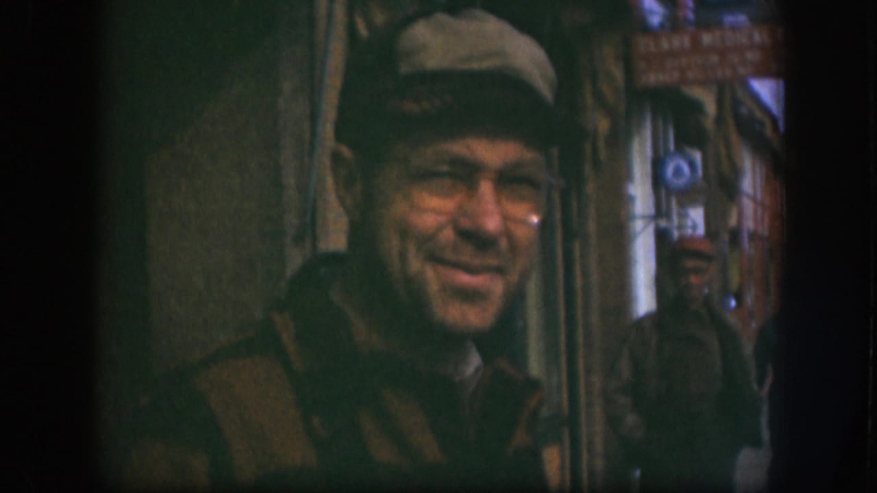 Near the end of the 1958 Kansas 8mm clip, the man in glasses turns slightly away from the camera in the narrow street passage.
