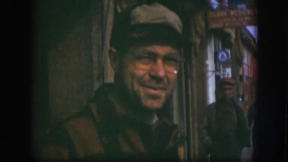 Near the end of the 1958 Kansas 8mm clip, the man in glasses turns slightly away from the camera in the narrow street passage.