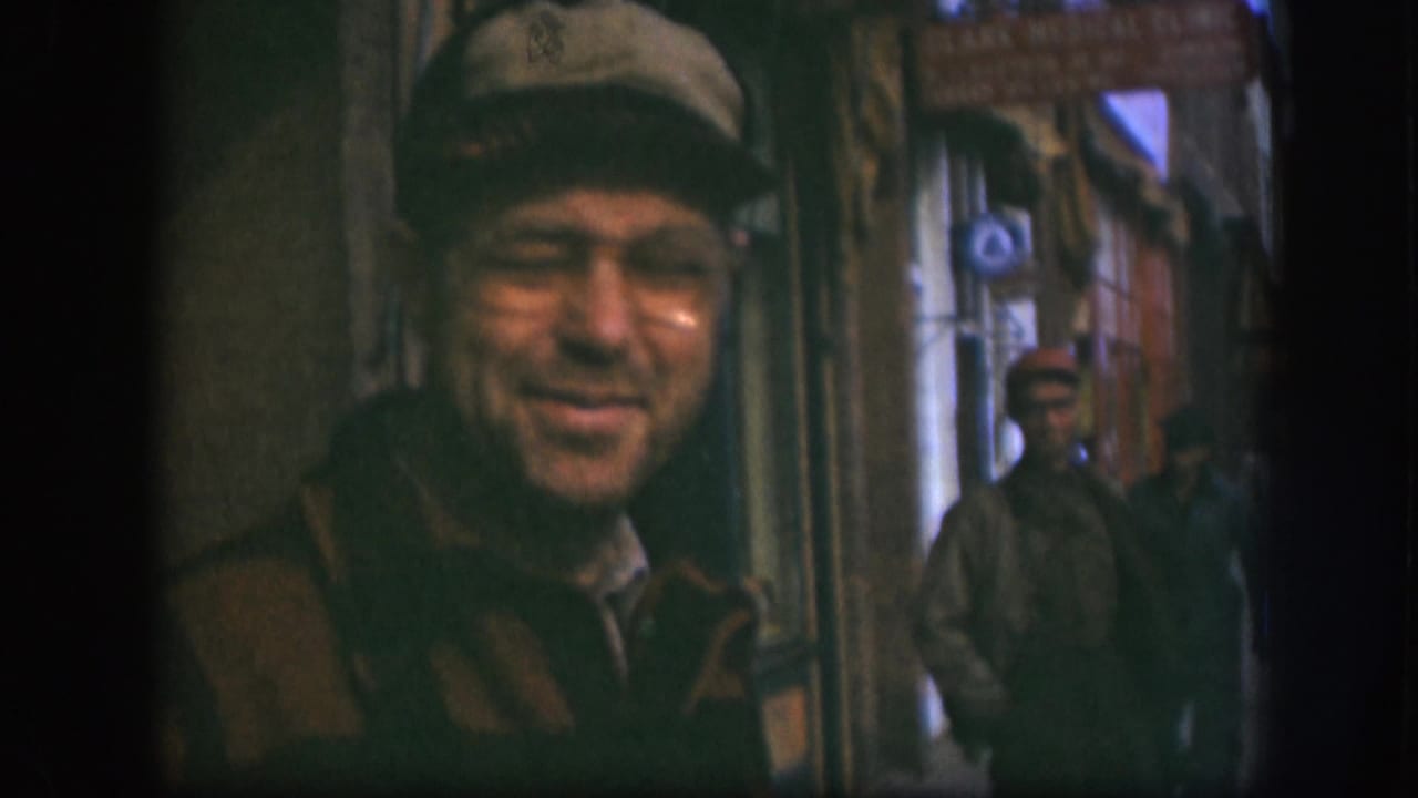The 1958 Kansas sidewalk view keeps the smiling man in glasses foregrounded, with a red-capped pedestrian and storefronts in the background.