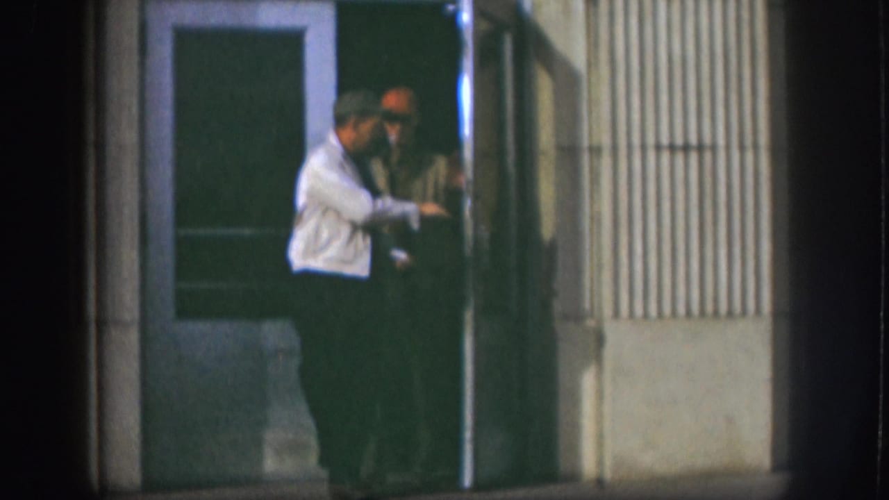 Two men stand close together in a dim doorway at night.
