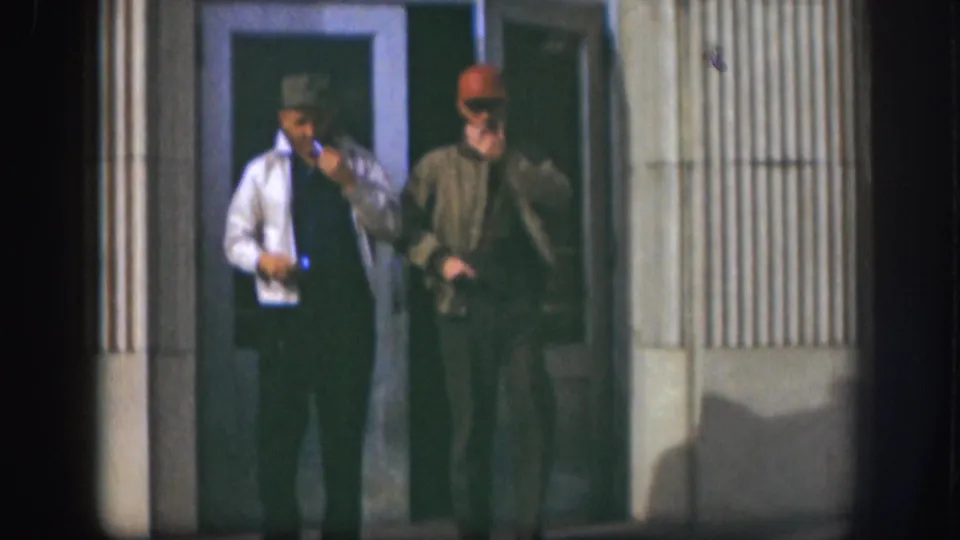 Two adult men in caps and jackets walk from a Kansas building entrance in 1958, with cigarettes visible in their hands.