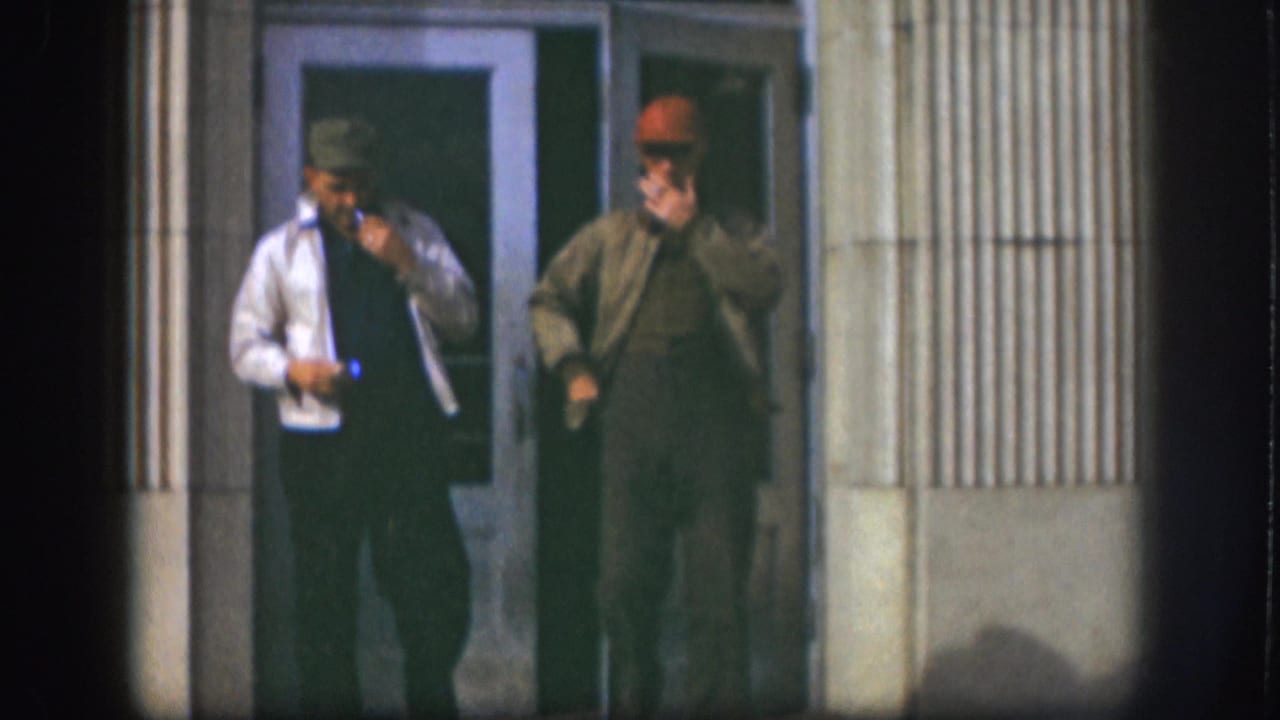 The 1958 Kansas frame shows two adult men smoking beside a doorway, one in a light jacket and one in a brown jacket.