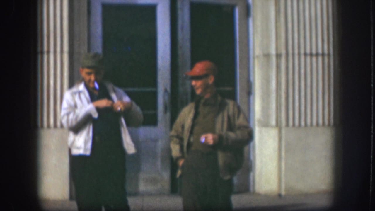 The 1958 Kansas footage shows two adult men outside glass doors, one adjusting his jacket as the other stands with a cigarette.
