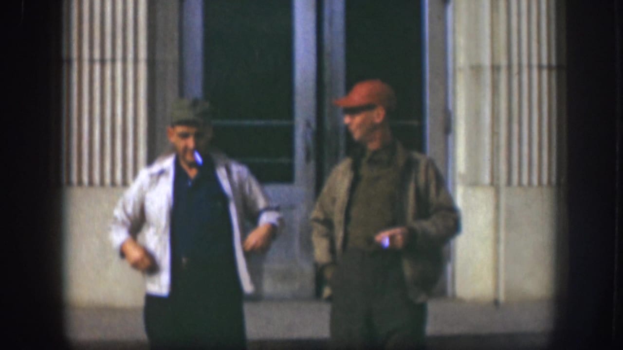 Two adult men in caps stand outside a columned building entrance.