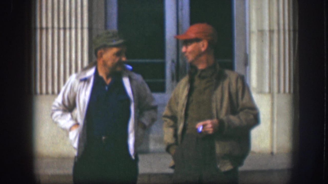 The 1958 Kansas 8mm frame shows two adult men continuing a casual cigarette-break conversation outside a building.