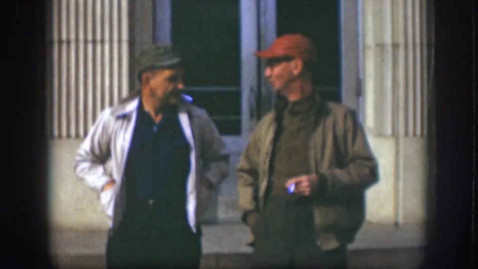 The 1958 Kansas 8mm frame shows two adult men continuing a casual cigarette-break conversation outside a building.