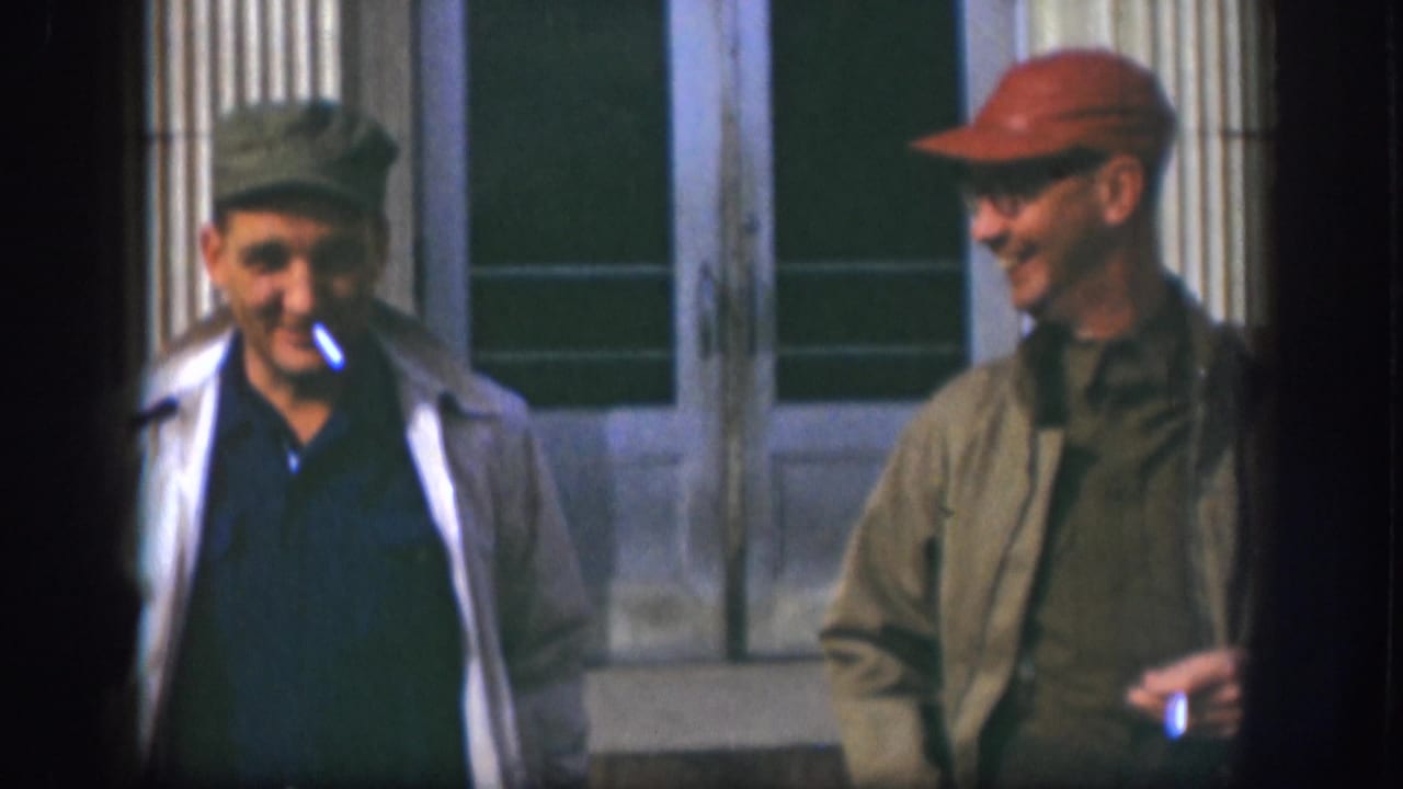Two adult men continue walking outside the Kansas building, with one smiling and the other holding a cigarette.