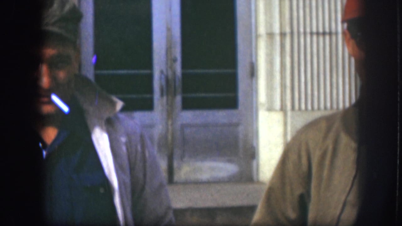 A close, partially cropped 1958 Kansas frame shows a man in a cap smoking, with another man partly visible beside him.