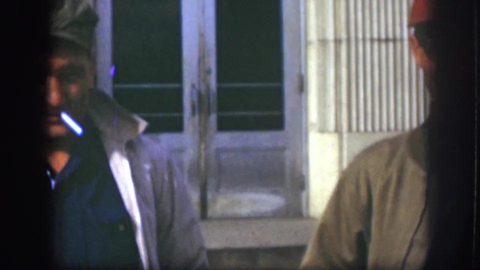 A close, partially cropped 1958 Kansas frame shows a man in a cap smoking, with another man partly visible beside him.