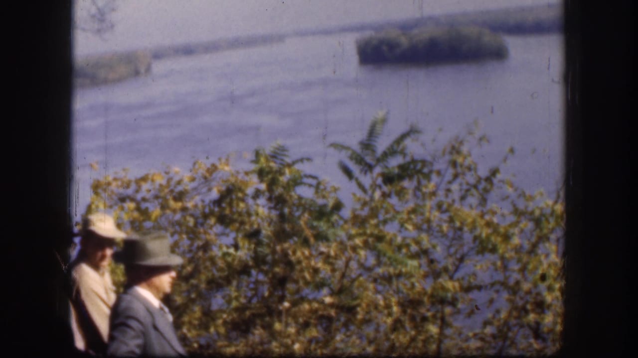 1958 Kansas 8mm frame showing two visitors in hats at a scenic overlook above a broad river or lake.