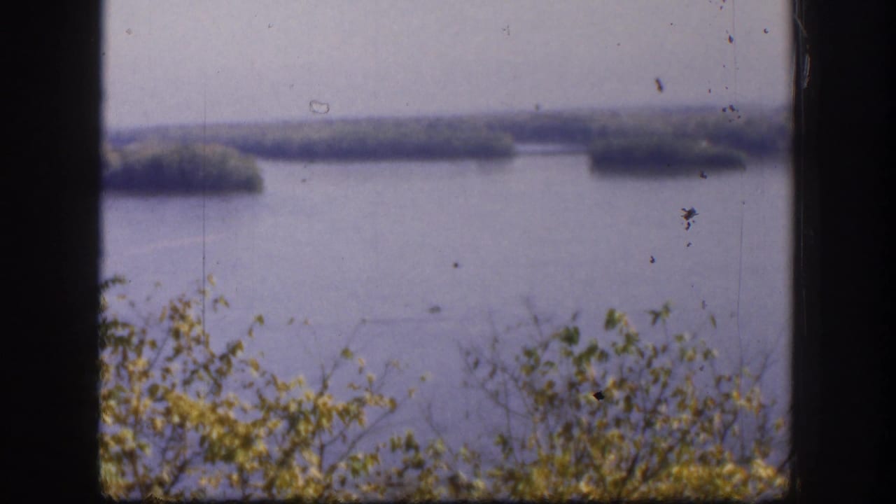 1958 Kansas 8mm frame with water, distant tree-covered islands, foreground brush, and heavy dark gate borders.