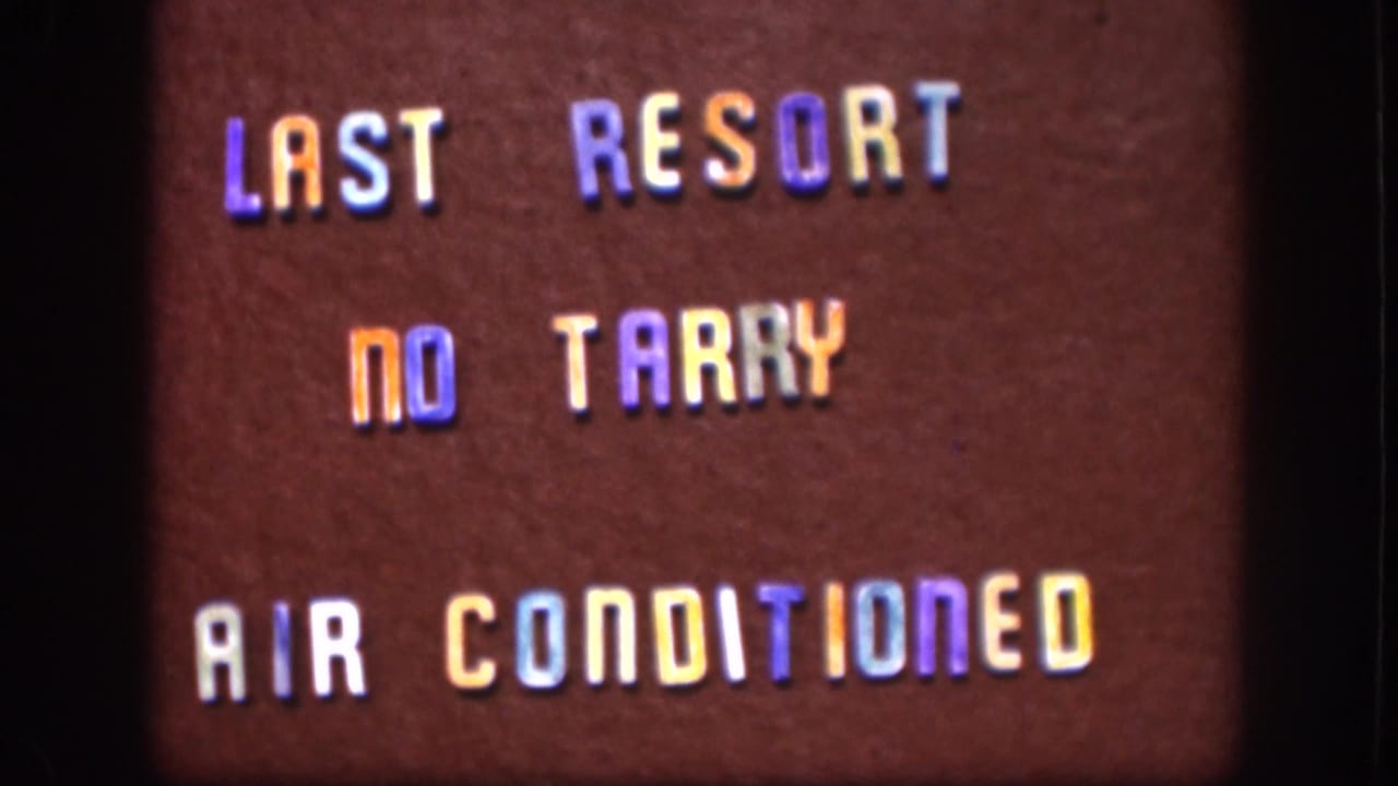 Close-up from 1958 Kansas home-movie footage showing a maroon sign with colored raised lettering and visible film grain.