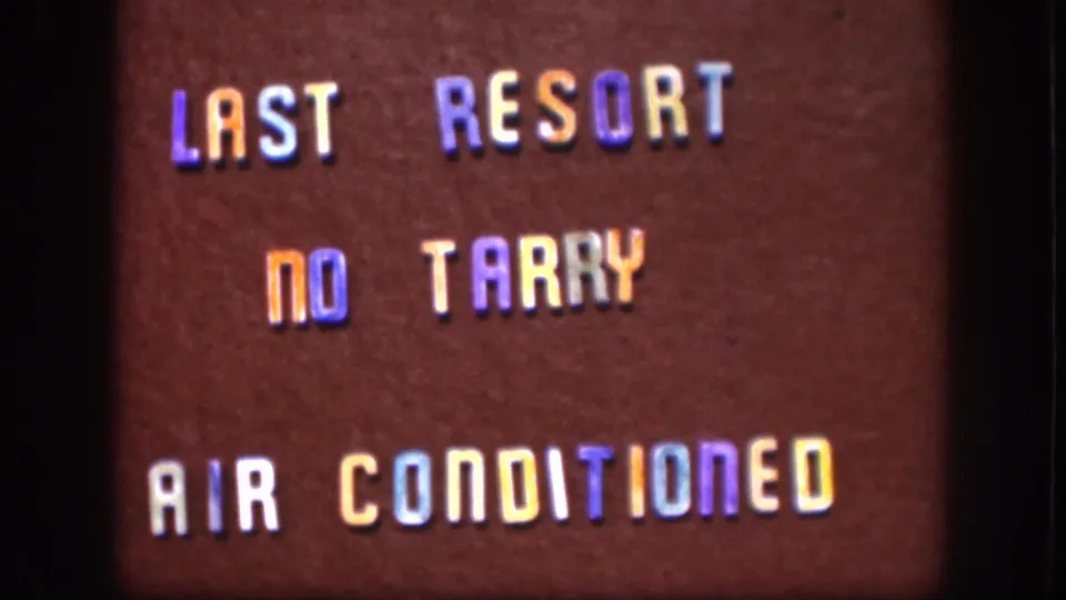 Close-up from 1958 Kansas home-movie footage showing a maroon sign with colored raised lettering and visible film grain.