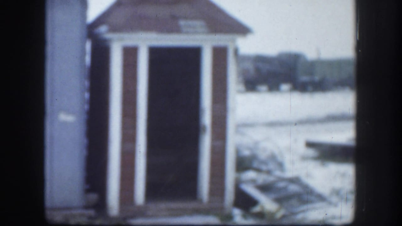 1958 Kansas 8mm frame showing a small rustic gabled building with white trim set in a snowy outdoor area.