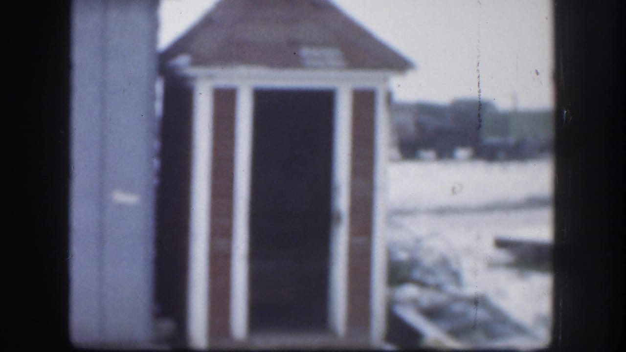 1958 Kansas 8mm frame of the same small gabled structure in snow, framed slightly off center with soft focus.