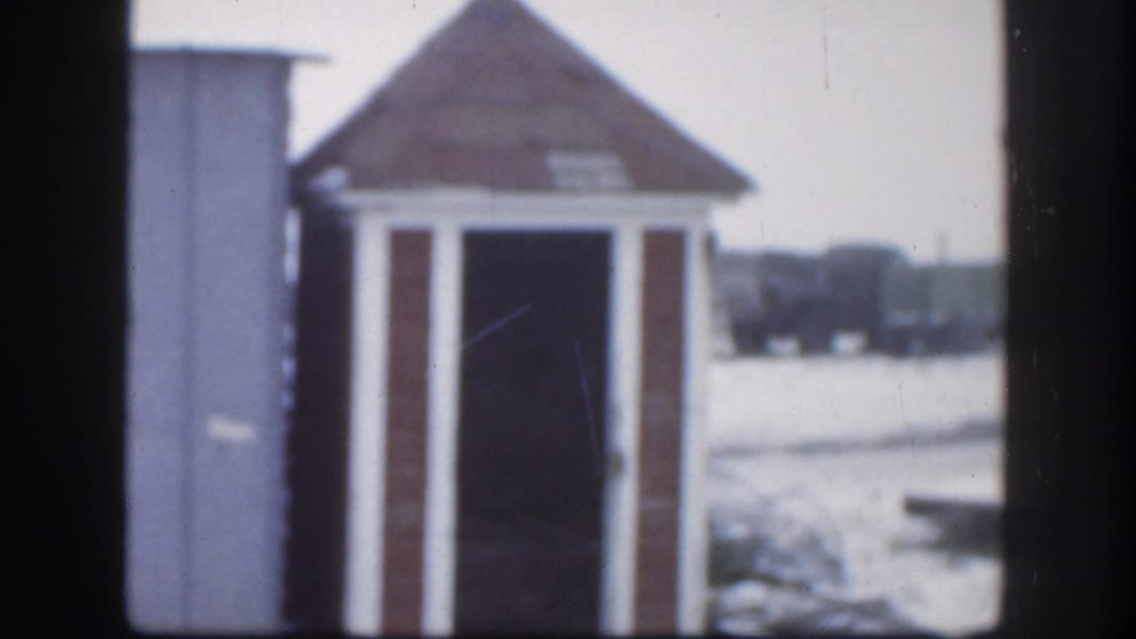 1958 Kansas 8mm frame showing a small brown shed with white trim beyond dark window-like framing and snow-covered ground.