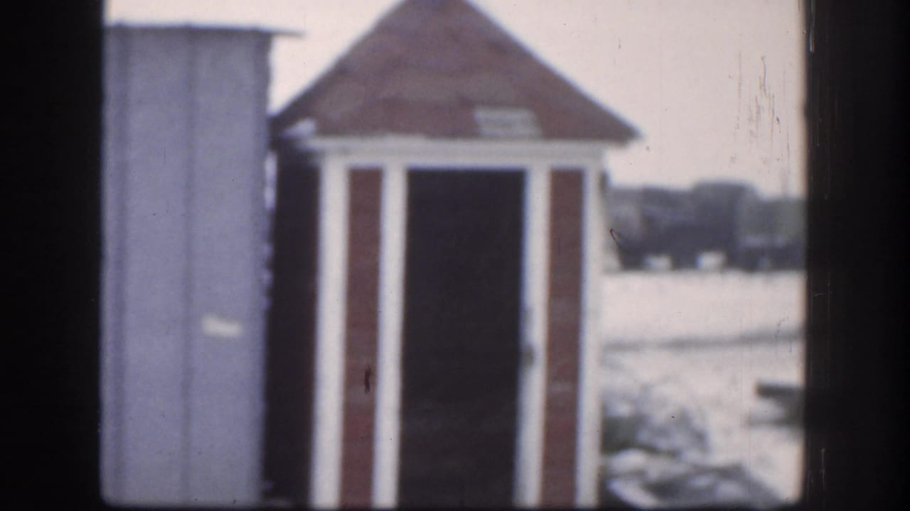 1958 Kansas home-movie frame with the shed centered between dark vertical edges and a snowy outdoor background behind it.