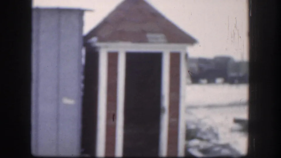 1958 Kansas home-movie frame with the shed centered between dark vertical edges and a snowy outdoor background behind it.