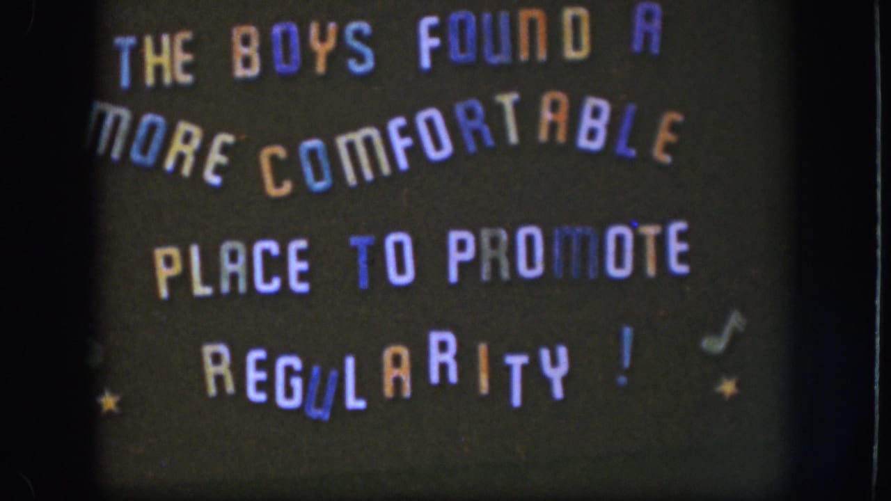 Final 1958 Kansas frame of the handmade comic sign, with arched text, colored letters, stars, and notes visible in soft focus.