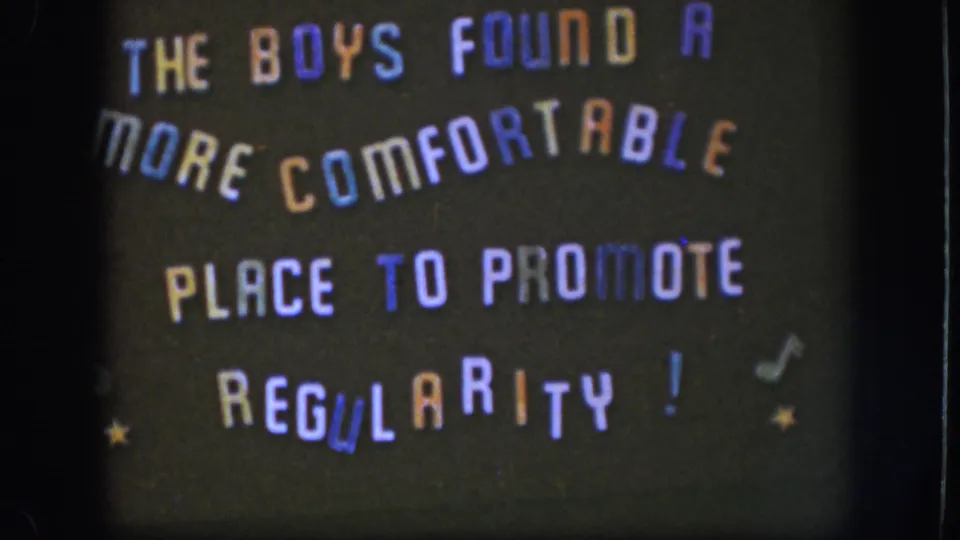Final 1958 Kansas frame of the handmade comic sign, with arched text, colored letters, stars, and notes visible in soft focus.
