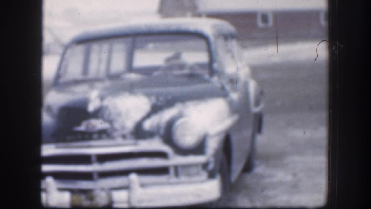 The front of the vintage car dominates the frame, showing snow on the hood and windshield area in a quiet 1958 Kansas winter yard.