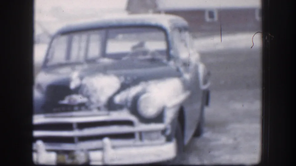 The front of the vintage car dominates the frame, showing snow on the hood and windshield area in a quiet 1958 Kansas winter yard.