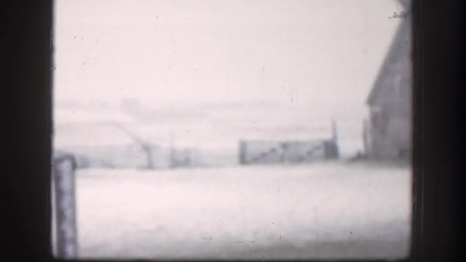 Soft 1958 Kansas farm view with snow-covered ground, distant buildings, and dark vertical framing in the foreground.
