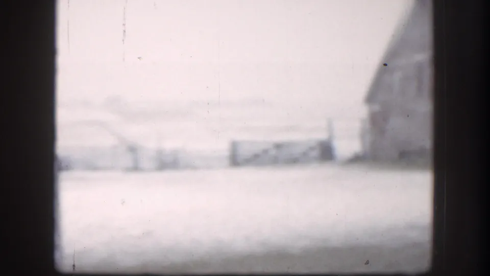 Snow-covered Kansas farmland with a distant barn-like building and pale sky, framed by dark vertical edges.