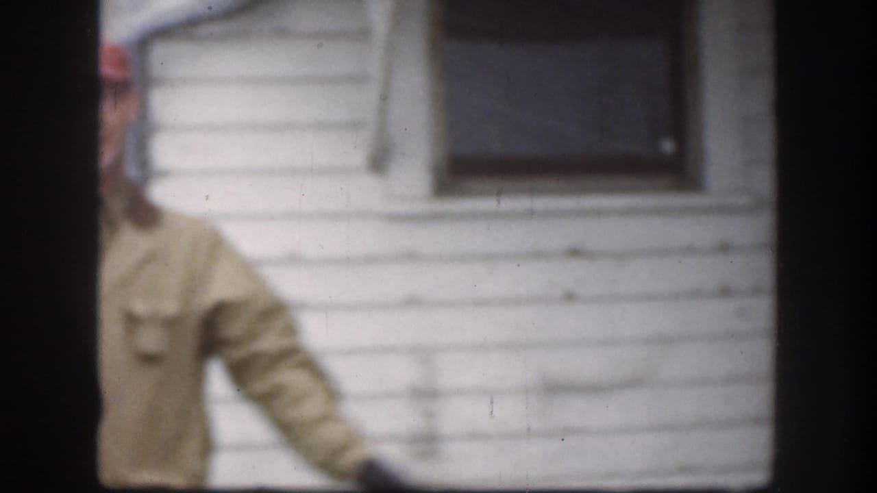 An adult man in a red cap and tan jacket stands beside the white-sided house, partly obscured by the contact-sheet frame division.