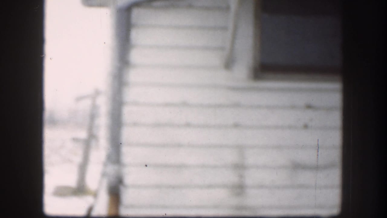 The final frame shows the white-sided house and dark window after the men have moved mostly out of view in the 1958 Kansas clip.