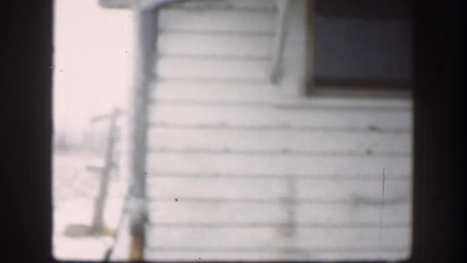 The final frame shows the white-sided house and dark window after the men have moved mostly out of view in the 1958 Kansas clip.