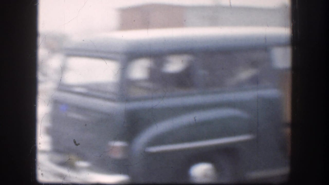 Soft 8mm frame of a dark mid-century car in snowy conditions, with window framing and faded color from the home-movie scan.